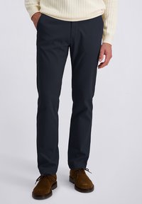 Marineblauwe broek van zacht, ademend materiaal, met een rechte pasvorm, voorzakken en een gladde afwerking. Gecombineerd met bruine schoenen.