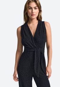 Mustmust mustriga sädelevast kangast. Omab sügavat V-kaelust, ilma varrukateta disaini ja ninaga talje detaili.