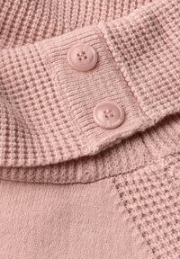 Suéter de punto rosa con un patrón de canalé texturizado, dos botones redondos y una tela suave en el escote.