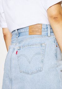Jeans alta vita di colore azzurro chiaro in denim, con una patch in pelle con il marchio e una linguetta rossa sulla tasca posteriore.