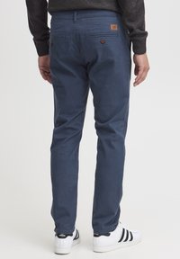 Pantalons en coton bleu marine à coupe droite, avec deux poches arrière à boutons et une petite étiquette de marque au-dessus d'une poche.