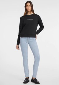 Mustad dressipluus tekstiga "GUESS JEANS", ümmarguse kaeluse ja soonikkoes mansettidega, kombineeritud helesiniste kitsaste teksade ja mustade paeltega kingadega.