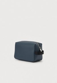 Mørkeblå kosmetiktaske med tekstureret overflade, rektangulær form, lynlåslukning og et sort stofhåndtag på siden.