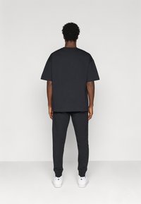 Czarny bawełniany t-shirt w oversize'owym rozmiarze z krótkim rękawem, sparowany z czarnymi dresami. Oba elementy odzieży charakteryzują się luźnym krojem i minimalistycznym stylem.