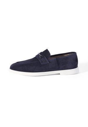 Mocassin en suède bleu marine avec détail de boucle argentée et semelle en caoutchouc blanche, présenté de profil sur fond blanc.