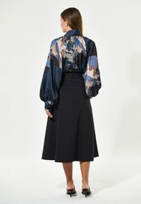 Silkkiblus med färgglada blommönster, voluminösa ärmar och en knytdetalj vid kragen, tillsammans med en högmidjad svart kjol.