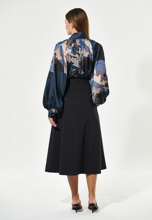 Seidene Bluse mit bunten Blumenmustern, voluminösen Ärmeln und einem gebundenen Kragen, kombiniert mit einem schwarz-hoch geschnittenen Rock.