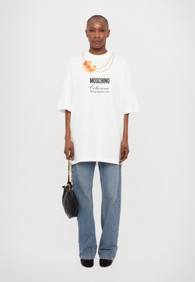 White oversized t-shirt with a graphic print of a pearl necklace and logo. Paired with light blue straight-leg jeans and a black handbag.
