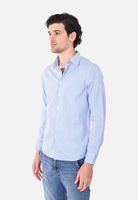 Camicia a maniche lunghe a righe blu e bianche con colletto button-down, vestibilità su misura e polsini singoli, abbinata a jeans blu.