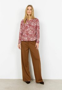 Červená kvetinová blúzka s dlhým rukávom v kombinácii so širokými hnedými nohavicami. Blúzka má golier a voľný strih; nohavice majú hladkú textúru.