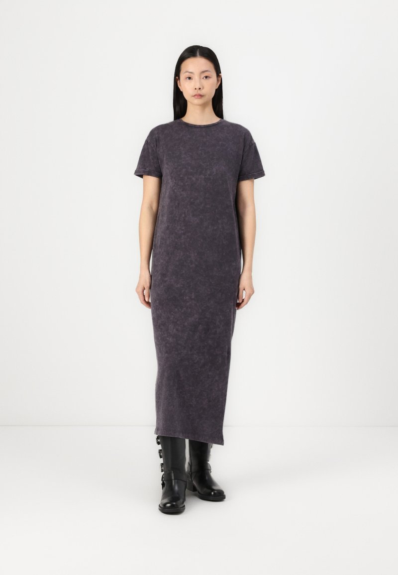Halli, pikk maxi-kleid, lühikeste varrukatega, valmistatud tekstuuriga kangast. Selga on pandud mustad kuni põlveni ulatuvad saapad, millel on rihmaaktsendid.