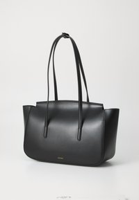 Sac fourre-tout en cuir noir avec une texture lisse, au design minimaliste, deux longues poignées et un discret logo doré en bas.