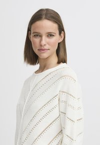 Weißer Strickpullover mit Zickzackmuster und Lochmuster-Akzenten. Rundhalsausschnitt und lange Ärmel mit lockerer Passform.
