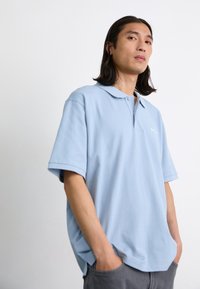 Polo light blue à manches courtes, col boutonné, fabriqué en tissu doux. Logo brodé discret sur la poitrine gauche.
