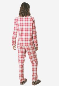 Completo pigiama in flanella a scacchi rossi e bianchi con maniche lunghe e pantaloni. Include dettagli in stile leopardato per le pantofole. Texture morbida e accogliente.