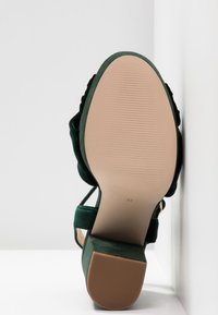 Sandale à talon en daim vert montrant une semelle beige lisse en taille 37 avec extrémité de talon en caoutchouc texturé sur fond blanc.