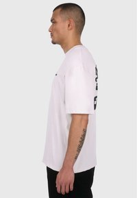 White oversized t-shirt with short sleeves, featuring black graphic print on the left side. Material appears soft and cotton-like.
