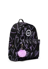 Musta reppu, jossa on violetteja sydänkuvioita, vetoketjullinen etutasku ja pörröinen violetti pom-pom-avainlenkki kiinnitettynä. Brändilogo edessä.