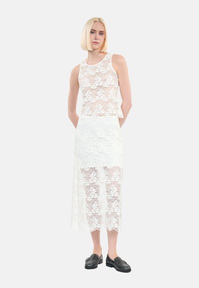Witte kant mouwloze top en midi rok set. Laagdesign met bloemmotieven, delicate textuur en gegolfde zoom. Zwarte instappers.