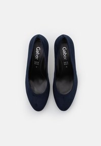 Ballerines en daim bleu marine avec bout arrondi et intérieur noir lisse. Présente un logo discret à l'intérieur ; design simple et épuré.