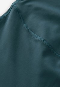 Gros plan d’un tissu bleu sarcelle montrant une texture lisse avec une couture visible cousue en diagonale.