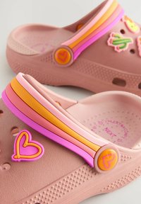 I zoccoli rosa presentano un design testurizzato, con diverse cinghie colorate (rosa, arancione) e decorazioni giocose tra cui forme di cuore e di cactus.
