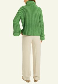 Grüner Strickpullover mit hohem Kragen und hochgekrempelten Ärmeln, kombiniert mit beigen Leinenhosen. Der Stoff weist ein strukturiertes, geripptes Muster auf.