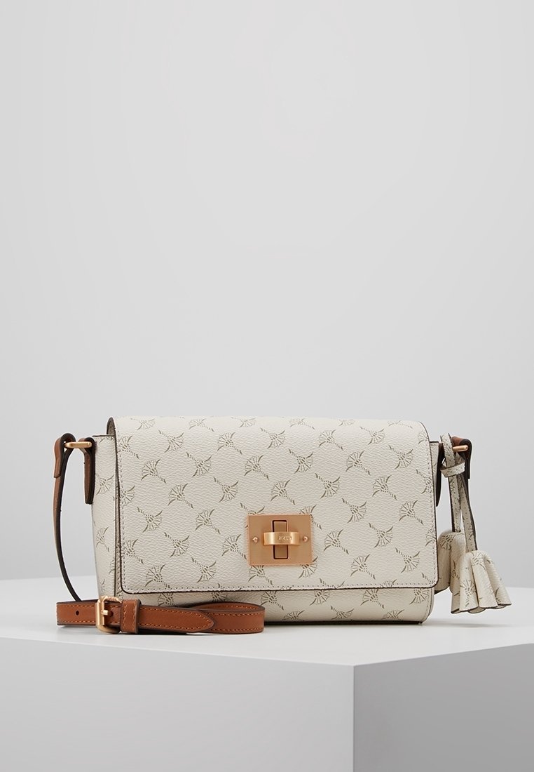 Cream-colored crossbody bag with textured finish, gold hardware, and a decorative tassel. Features a patterned design and adjustable strap.