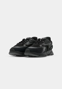 Zapatillas negras con parte superior de malla, suela de goma y acentos texturizados. Incluyen cordones y un collar acolchado para mayor comodidad.