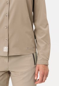 Camicia button-up beige realizzata in tessuto leggero, con logo e etichetta di materiali riciclati. Maniche lunghe e texture morbida; design aderente.