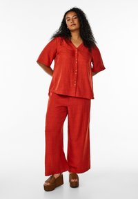 Top in lino rosso con maniche corte e chiusura a bottoni, abbinato a pantaloni larghi coordinati. Accentuato da sandali platform in woven.