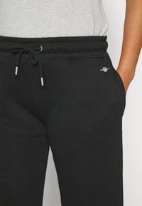 Schwarze Jogginghose mit elastischem Bund, Kordelzug und Taschen. Mit einem kleinen, gestickten Logo auf der linken Seite. Weicher Stoff.