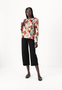 Blomstertrykt bluse med lange ermer i oransje, rosa og grønne nyanser, kombinert med svarte, korte bukser. Svarte flate sandaler med spenne.
