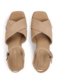 Μπεζ σανδάλια με τακούνι από σουέτ, ανοιχτό δάχτυλο, λουριά που διασταυρώνονται και ρυθμιζόμενο λουράκι στον αστράγαλο με εξαρτήματα σε χρυσό τόνο.