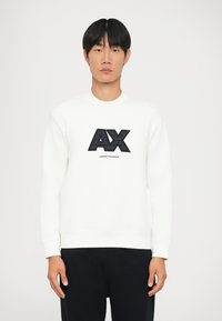 Fehér pulóver bordázott mandzsettákkal és hem, nagy fekete "AX" logóval és az "ARMANI EXCHANGE" felirattal alatta. Simaszövet.