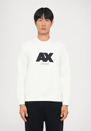 Balti džemperis su nertomis rankogaliais ir apvadu, su dideliu juodu "AX" logotipu ir tekstu "ARMANI EXCHANGE" atspaudintu žemiau. Lygi tekstūra.