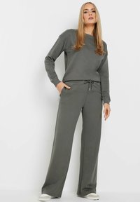 Grijze sweatshirt en bijpassende jogger set gemaakt van zachte stof. De trui heeft een ronde halslijn en een ontspannen pasvorm. De broek heeft een koord in de taille.