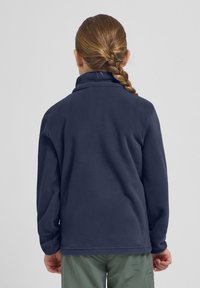 Tumed fliisist pullover kõrge kraega, pikad varrukad ja pehme tekstuur, kantud helesiniste cargo-lühikeste pükstega.
