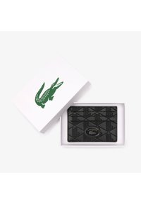 Porte-cartes en cuir noir avec motif géométrique en relief, arborant un logo Lacoste argenté et présenté dans une boîte blanche avec un logo crocodile vert.
