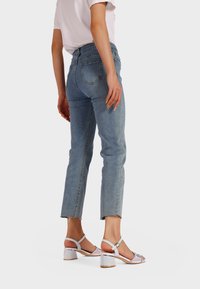 Jeans a vita alta di colore blu chiaro con una vestibilità affusolata, caratterizzati da orli sfilacciati e due tasche posteriori. Abbinati a sandali con tacco argento.