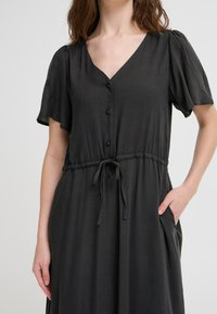 Abito grigio a maniche corte con scollatura a V, bottoni frontali, cintura elastica e tasche laterali. Tessuto liscio con una vestibilità comoda.