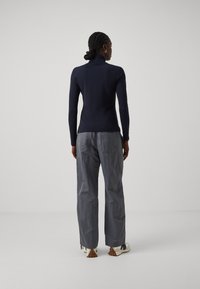 Marineblauer Rollkragenpullover mit langen Ärmeln, kombiniert mit lockeren grauen Hosen. Glatte Textur mit minimalistischem Design und subtilen Hardware-Details.