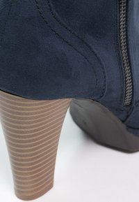 Botte cheville en suède bleu avec un talon empilé texturé marron, fermeture éclair sur le côté et coutures détaillées le long de la partie supérieure.