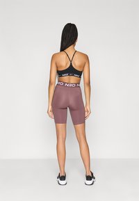 Must värviga spordibrasiil, millel on "NIKE" brändi logo, koos kehakujuliste burgundi värvi jalgrattapükstega, millel on "NRO" vöökoht. Taustal on ühtlane taust.