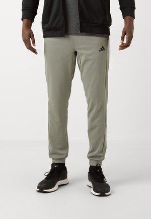 Sivo-zeleni atletski hlače s elastičnim manžetama, bočnim trakama i Adidas logom. Uparen s crnim tenisicama za trčanje koje imaju bijele potplate.