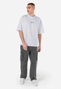 Witte t-shirt met korte mouwen met het "PEGADON" logo in het zwart. Combinatie met grijze cargo-broeken met zijzakken en witte sneakers.
