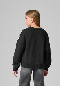 Svart oversized sweatshirt med ribbade mudd och nederkant, med en minimalistisk design. Bärs med blekgrå byxor.