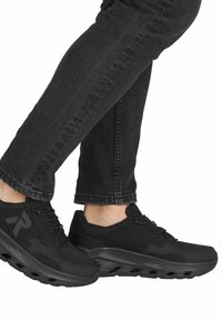 Černé sportovní boty s prodyšným svrškem, polstrovanou podešví a šněrováním, v kombinaci s tmavými džíny, zobrazené zblízka.