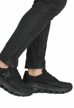Czarne buty sportowe z siateczkową górą, amortyzowaną podeszwą i sznurowadłami, połączone z ciemnymi dżinsami, przedstawiające zbliżenie na obuwie.