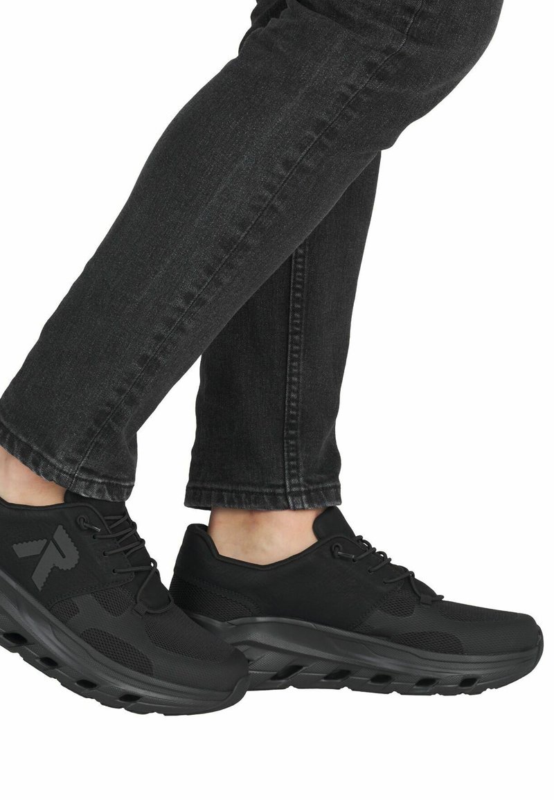 Černé sportovní boty s prodyšným svrškem, polstrovanou podešví a šněrováním, v kombinaci s tmavými džíny, zobrazené zblízka.